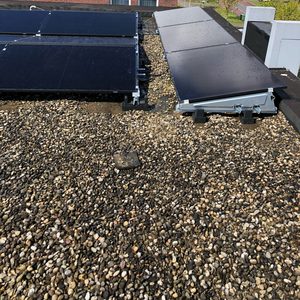 De afbeelding toont een reeks zonnepanelen op een plat dak, met een zichtbaar grindbed en omliggende gebouwen op de achtergrond.