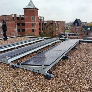 De foto toont zonnepanelen geïnstalleerd op een dak met grindbedekking. Een technicus is bezig met de installatie.