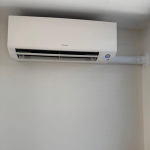 De afbeelding toont een wand-airconditioner geïnstalleerd aan de muur, met een eenvoudige en moderne uitstraling.