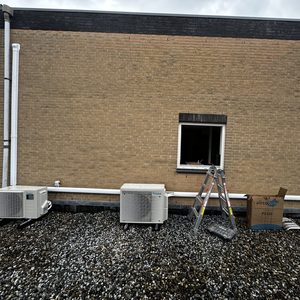 Twee airco-units zijn geïnstalleerd op het dak met leidingen naar het binnengebied. Een ladder staat klaar voor verdere werkzaamheden.
