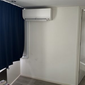 De afbeelding toont een wandunit voor airconditioning, geïnstalleerd in een moderne ruimte met een neutrale interieurstijl.