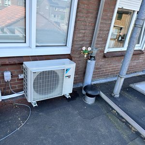 De afbeelding toont een buitenunit van een airconditioninginstallatie. Er zijn twee units zichtbaar, met bijbehorende leidingen en aansluitingen.