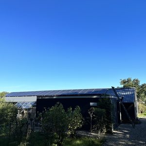 Deze afbeelding toont een woning met zonnepanelen op het dak, omringd door groen en een heldere blauwe lucht.