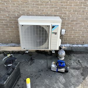 De afbeelding toont een airconditioningsysteem van het merk Daikin, geïnstalleerd aan een muur met bijbehorende apparatuur en accessoires.