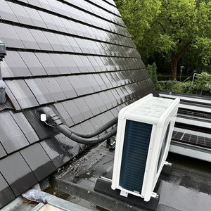 Installatie van een warmtepomp op een dak, met zichtbare aansluitingen en zonnepanelen op de achtergrond.