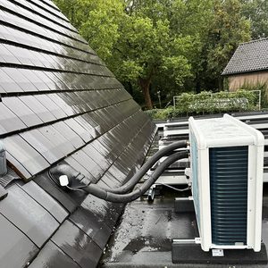 De foto toont een airconditioningunit geïnstalleerd op een dak met gebruikelijke afvoerslangen en een modern ontwerp.