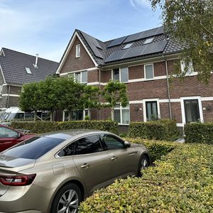 De afbeelding toont zonnepanelen geïnstalleerd op het dak van een woning, met een heldere blauwe lucht op de achtergrond.