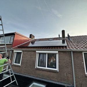 Een installatie van zonnepanelen op een hellend dak met een werknemer die een ladder gebruikt voor de werkzaamheden.