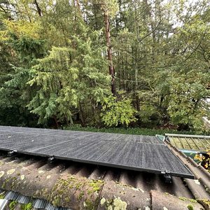 Een installatie van zonnepanelen op een hellend dak, omgeven door bomen, die waarschijnlijk stroom opwekt uit zonne-energie.