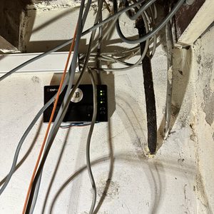 De foto toont een deel van de bekabeling van een zonnepanelensysteem, inclusief een omvormer met indicatorlampjes.
