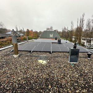De foto toont zonnepanelen op een plat dak, omringd door grind. De installatie is duidelijk zichtbaar met meerdere panelen die zijn geplaatst.