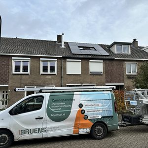 De foto toont een woning met zonnepanelen op het dak en een installatievoertuig van een zonnepaneelbedrijf ervoor.