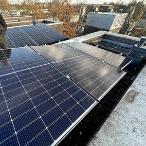 Een installatie van zonnepanelen op een plat dak, met een technicus die een van de panelen inspecteert.