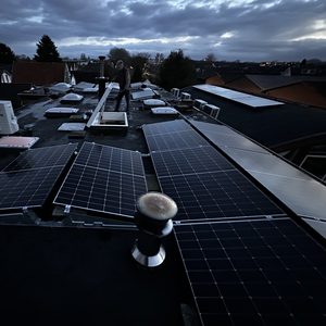 De installatie toont zonnepanelen op een dak, met enkele andere apparaten in de omgeving. De foto is in de schemering genomen.
