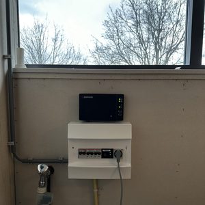 De afbeelding toont een monitoring unit voor een zonnepaneleninstallatie, waarbij elektrische componenten zijn verbonden met de meterkast.
