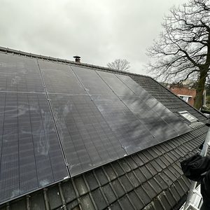 Installatie van zonnepanelen op een hellend dak, zichtbaar onder een bewolkte lucht.