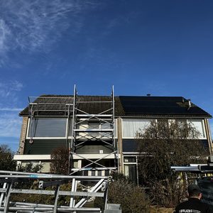 De afbeelding toont een woning met zonnepanelen op het dak, met steigerwerk voor installatie of onderhoud.