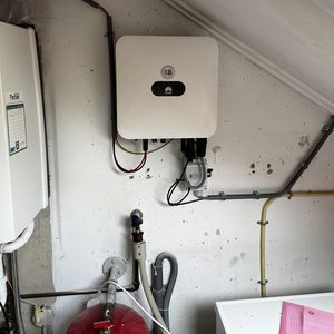 De installatie toont een omvormer voor zonnepanelen, welke de gelijkstroom van de panelen omzet in wisselstroom voor huishoudelijk gebruik.