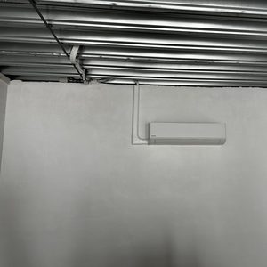 Een wandmodel airconditioningseenheid is geïnstalleerd op een gladde wand, met zichtbare leidingen die de stroomvoorziening en afvoer ondersteunen.