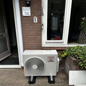Een buitenunit van een airconditioning systeem geplaatst tegen de muur van een huis, met de nodige ondersteuning en installatiecomponenten.