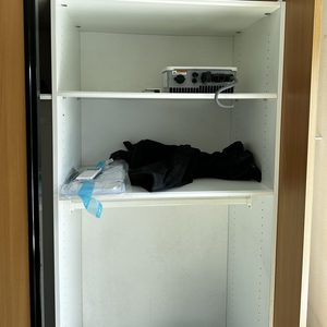 Een airconditioning unit is geplaatst in een kast met enkele accessoires en kleding. De installatie is ordelijk en professioneel gepresenteerd.