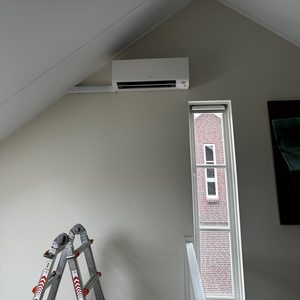De afbeelding toont een geïnstalleerde airconditioningseenheid bevestigd aan de muur in een kamer met een hellend plafond.