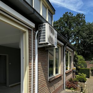 Een airco-installatie is zichtbaar aan de buitenkant van een woning, leidingen zijn aangesloten en de unit is stevig bevestigd.