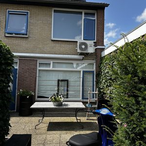 De afbeelding toont een airconditioningseenheid bevestigd aan de muur van een woning, met een tuinset op de voorgrond.