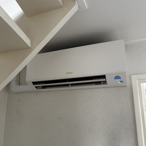 Een wandunit van een airconditioningsysteem bevestigd aan de muur, voorzien van een blauwe indicatielamp.