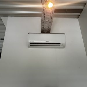 De foto toont een wandgemonteerde airconditioningseenheid tegen een witte muur, met een ladder eronder voor installatie.