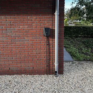 De afbeelding toont een laadpaal voor elektrische voertuigen bevestigd aan een muur, met kabels die de verbinding met het elektrische systeem aangeven.