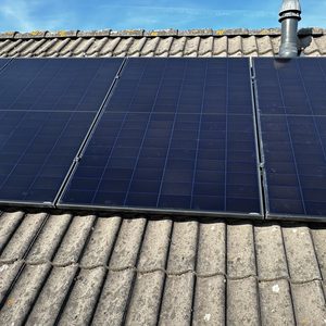 Een installatie van zonnepanelen op een hellend dak, zichtbaar met meerdere panelen en een blauwe lucht op de achtergrond.