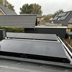 De foto toont een installatie van zonnepanelen op een hellend dak, met een technicus die de panelen controleert.