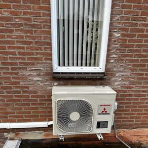 Een buitenunit van een airconditioning met een ventilator, geïnstalleerd op een muur, met leidingen zichtbaar.