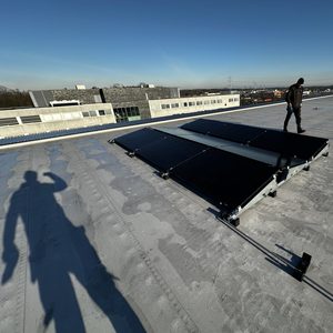 Een zonnepaneelinstallatie op een plat dak met enkele panelen en een monteur aan het werk.