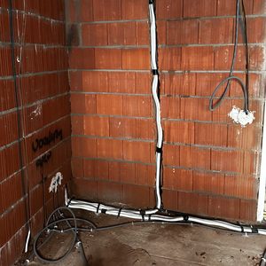De foto toont de installatievoorbereiding voor een airconditioning systeem, met elektrische bekabeling en leidingen in een ruwe muuromgeving.