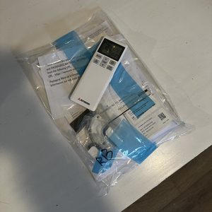 De foto toont een afstandsbediening voor een airconditioning apparaat, omgeven door documentatie en verpakkingsmateriaal.
