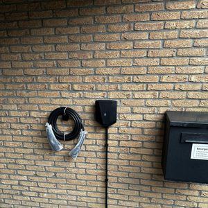 Een laadpaal aanwezig aan de muur, met een kabel en enkele accessoires ernaast.