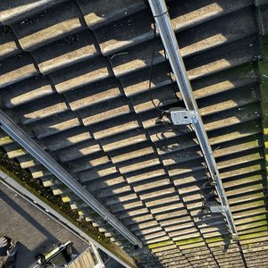 De foto toont een gedeelte van de installatie van zonnepanelen op een hellend dak met bevestigingssystemen en bekabeling.