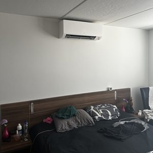 Een wandunit voor airconditioning is gemonteerd boven het bed in een slaapkamer.