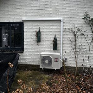 Deze afbeelding toont een buitenunit van een airconditioning systeem, netjes bevestigd aan een witte muur.