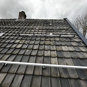 De foto toont een gedeeltelijke installatie van zonnepanelen op een schuin dak met montagesystemen en bekabeling.