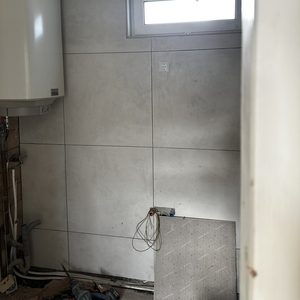 De foto toont een meterkast met elektrische bedrading en een waterverwarmer. De ruimte lijkt in aanbouw en is nog niet volledig afgewerkt.