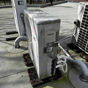 Een buitenunit van een airconditioningsysteem, geïnstalleerd op een plat dak met zichtbare leidingen en aansluitingen.