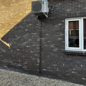 Een wandgemonteerde airconditioningseenheid bevestigd aan een bakstenen muur, met leidingen zichtbaar die de verbinding maken.