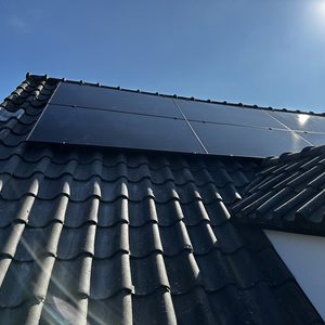 De afbeelding toont zonnepanelen op een hellend dak, met een heldere lucht op de achtergrond.