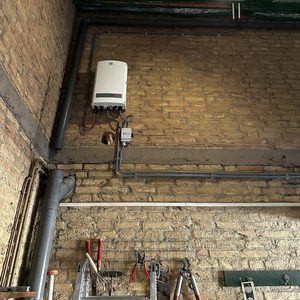 Installatie van een omvormer voor zonnepanelen, zichtbaar boven de leidingen in een wand. Gereedschap en materialen zijn ook aanwezig.