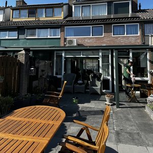 Een airco-installatie op de buitenmuur van een woning, zichtbaar boven de patio, met een helder blauwe lucht op de achtergrond.