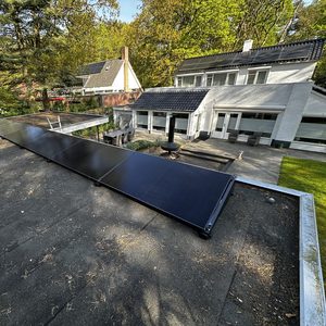 De afbeelding toont zonnepanelen die zijn geïnstalleerd op het dak van een woning, omgeven door een groene omgeving.
