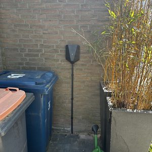 Een laadpaal voor elektrische voertuigen, netjes geïnstalleerd aan een bakstenen muur, omringd door andere objecten in de tuin.